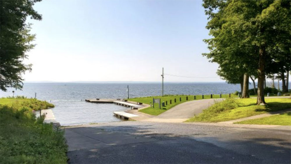 Godfrey Point boat launch with trees on the left and right, green grass on each side of the concrete going into the water at Oneida Lake
